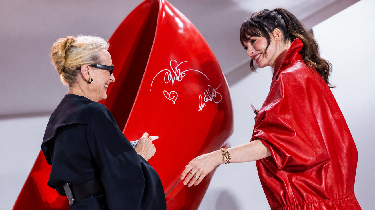 Duas mulheres a sorrir enquanto fazem autógrafos numa grande escultura vermelha.